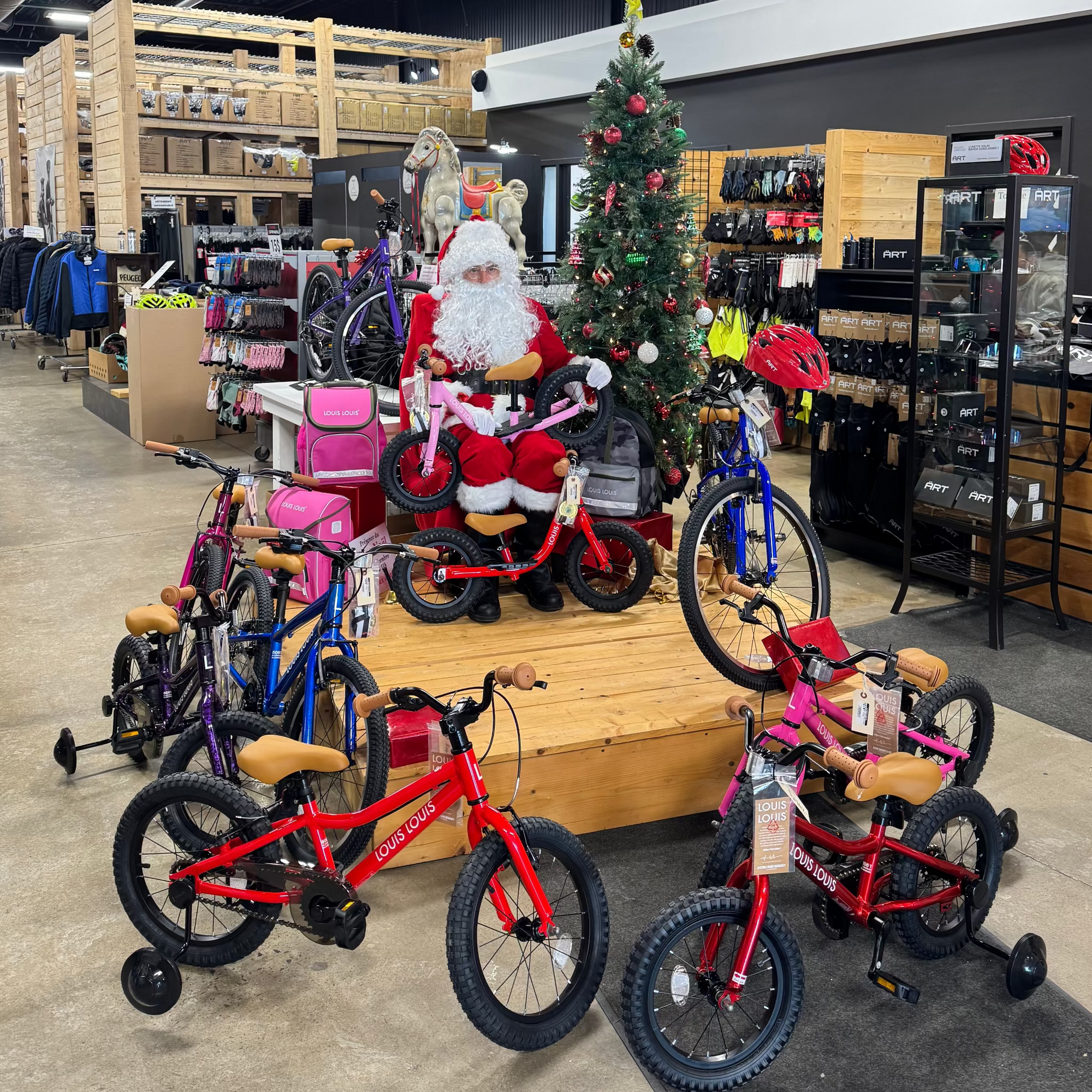 LOUIS LOUIS Kids' Bikes displayed in a store with a person dressed as Santa Claus.